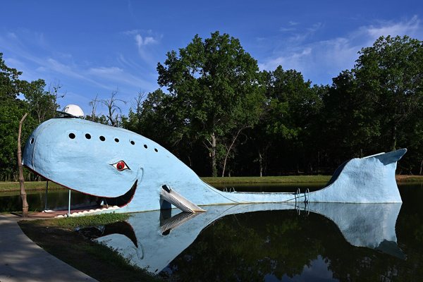 The Blue Whale of Catoosa reflected in its pond beneath a blue sky