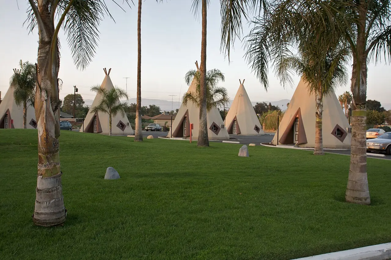 Tipi-shaped rooms of the Wigwam Motel behind a lawn and palm trees